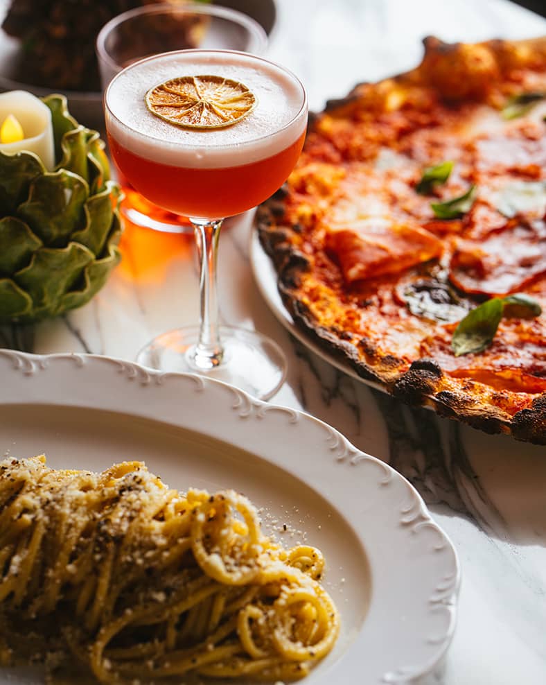 Macro shot of a table with various Italian foods and cocktails.